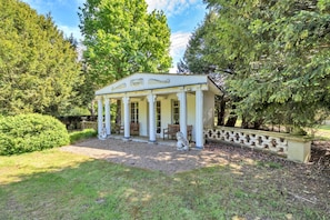 Um gazebo branco com colunas e teto, cercado por árvores e um caminho de cascalho.