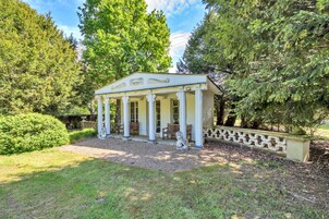 Um gazebo branco com colunas e teto, cercado por árvores e um caminho de cascalho.