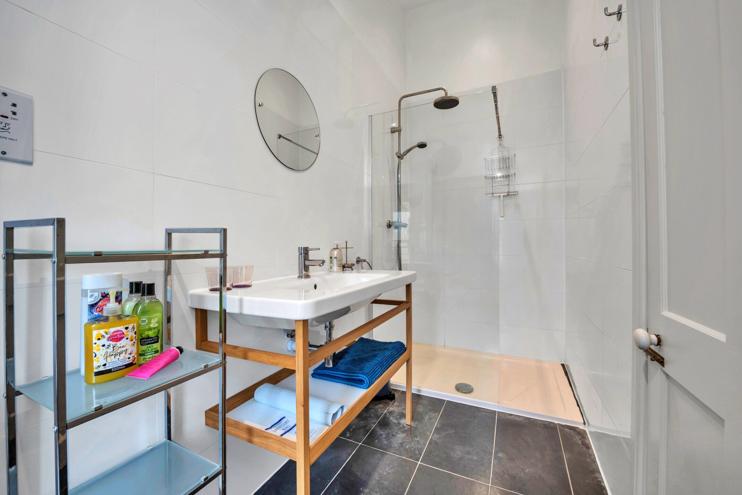 Une salle de bain moderne avec une douche à l’italienne en verre, un lavabo blanc avec un meuble-vasque en bois et un miroir au mur.