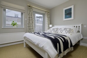 Un dormitorio con cama, ventana con cortinas, radiador y una lámpara fijada a la pared.