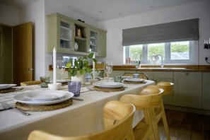 Un comedor con una mesa dispuesta para cuatro, sillas de madera, una ventana con vistas y una cocina al fondo.