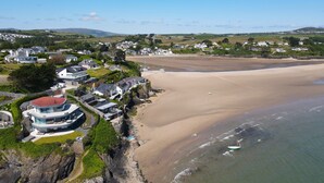 A coastal residential area with houses along the beach, a sandy beach, and a rocky cliff. - Stylish Barn Retreat for 8 (Pwllheli)