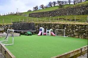 Ein Spielplatz mit Kunstgrashalm, einer Rutsche und einer Kletteranlage.