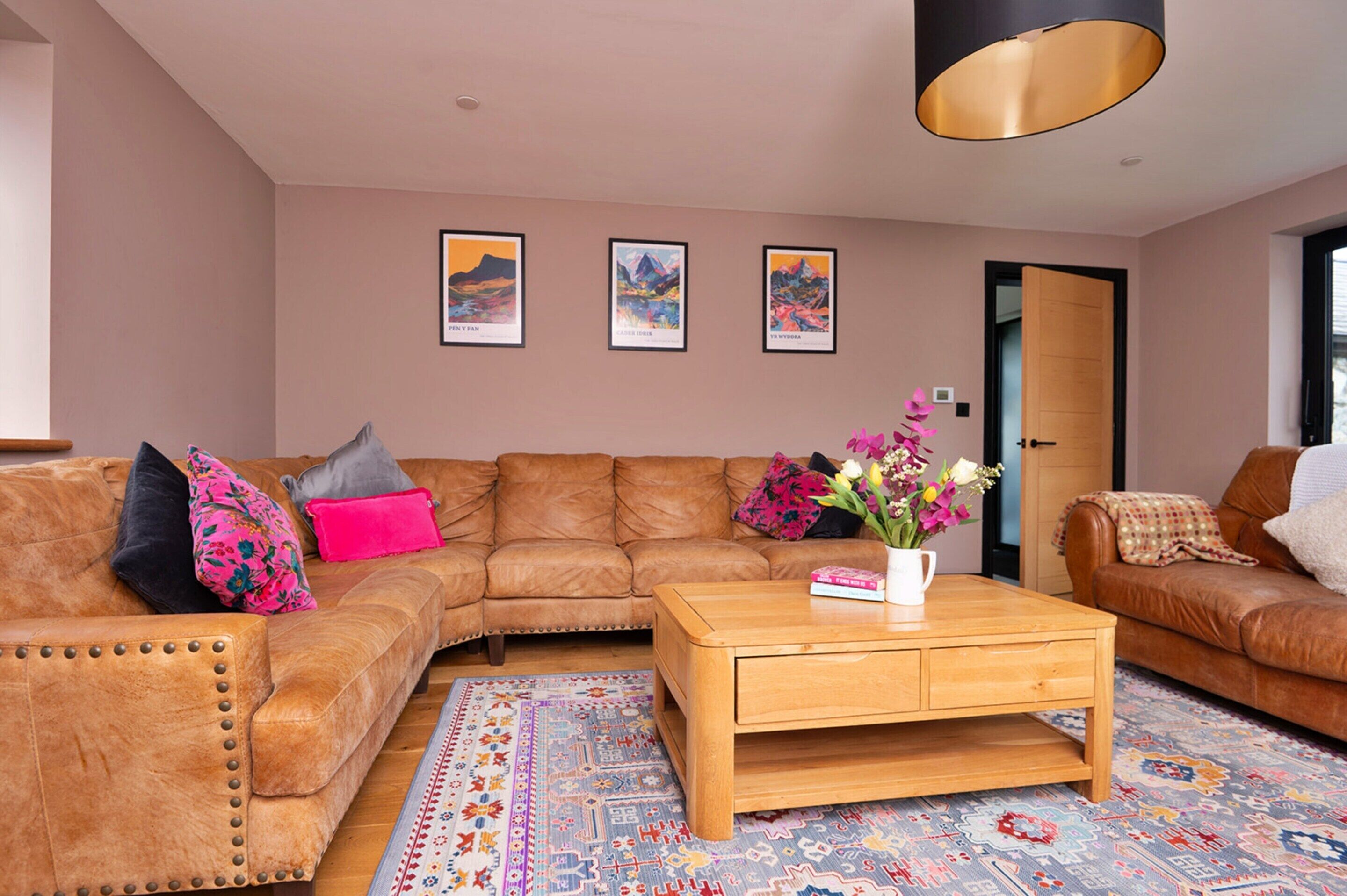 A living room with a brown leather sofa, a wooden coffee table, and a colorful rug. There are three framed pictures on the wall.