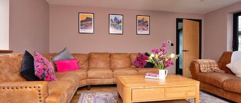 A living room with a brown leather sofa, a wooden coffee table, and a colorful rug. There are three framed pictures on the wall.