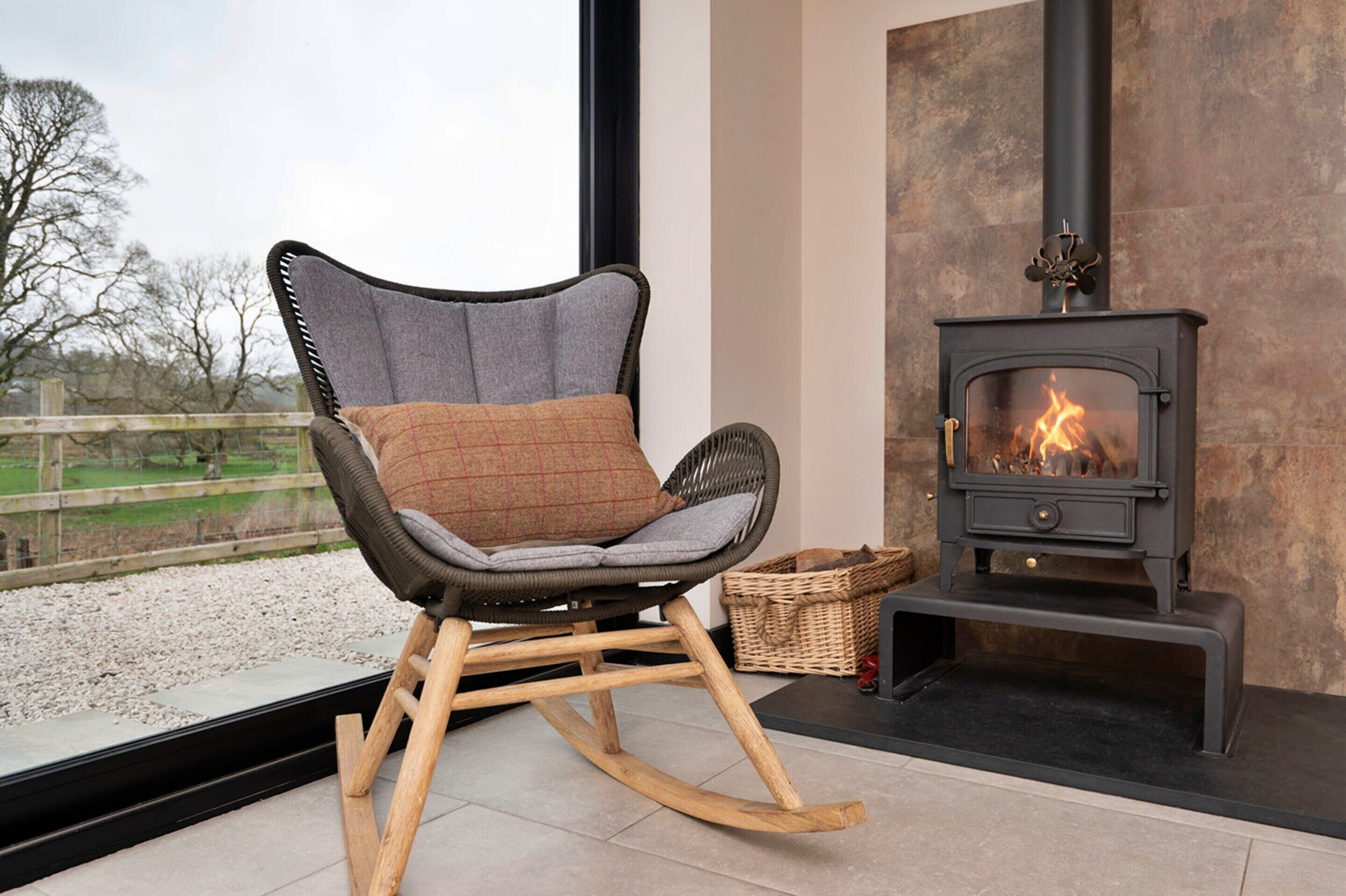 Un fauteuil à bascule avec un coussin, une cheminée et une vue sur l’extérieur.