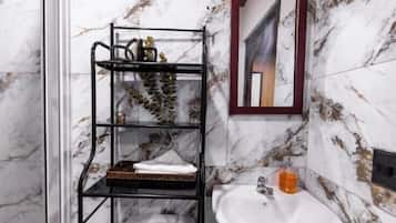 Un baño con pared de mármol, un estante de metal negro con toallas, un lavabo y un espejo.