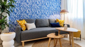Un salon moderne avec un canapé gris, des coussins jaunes et bleus, une petite table en bois et un lampadaire.