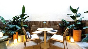 Un espace de détente extérieur accueillant, avec une table ronde et quatre chaises, entouré de grands pots de plantes et d’une clôture en bambou.