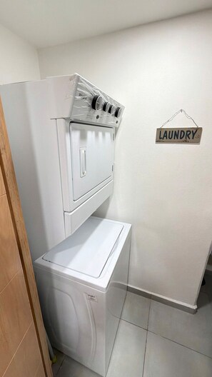 A laundry room with a stacked washer and dryer, a sign indicating the room's purpose, and a tiled floor. - One-of-a-Kind Venue: Akron World Stadium 2026 (Zapopan)