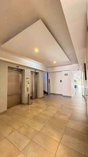 A spacious hallway with two elevators, a trash bin, and a clear path leading to an exit. - One-of-a-Kind Venue: Akron World Stadium 2026 (Zapopan)