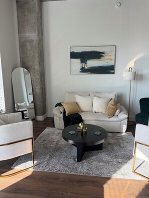 A modern living room with a white sofa, a round coffee table, and a large abstract painting on the wall. - 3-bedroom apartment in soothing Birmingham with AC comfort (Birmingham)