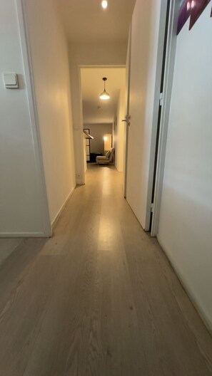 Ein Flur mit Holzboden, der zu einem Zimmer mit Bett und Stuhl führt.
