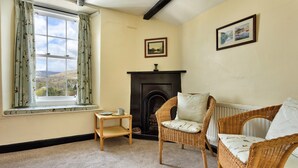 A cozy room with a fireplace, two wicker chairs, a small table, and a window with curtains. - Charming Snowdonia Cottage for 4 (Ambleside)