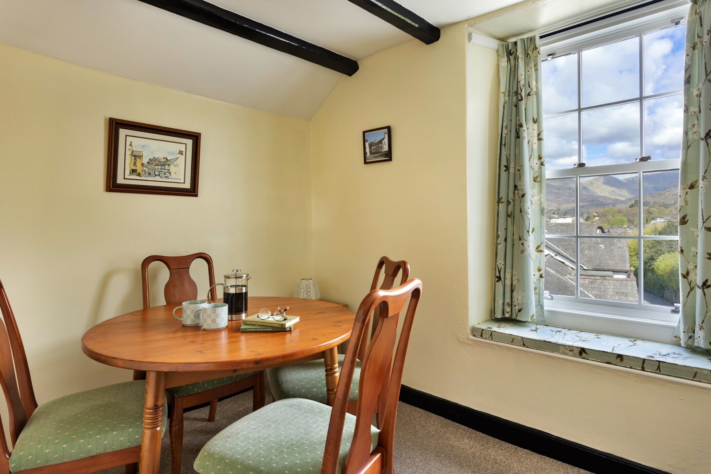 A dining area with a wooden table, chairs, and a window with a view of the countryside.