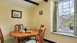 A dining area with a wooden table, chairs, and a window with a view of the countryside. - Charming Snowdonia Cottage for 4 (Ambleside)