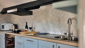 A kitchen with a microwave, a kettle, a wine bottle, and a rolling pin on the counter. - Charming Snowdonia Cottage for 4 (Ambleside)