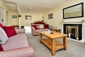 A living room with a sofa, a wooden coffee table, a fireplace, and a mirror on the wall. - Charming Snowdonia Cottage for 4 (Ambleside)