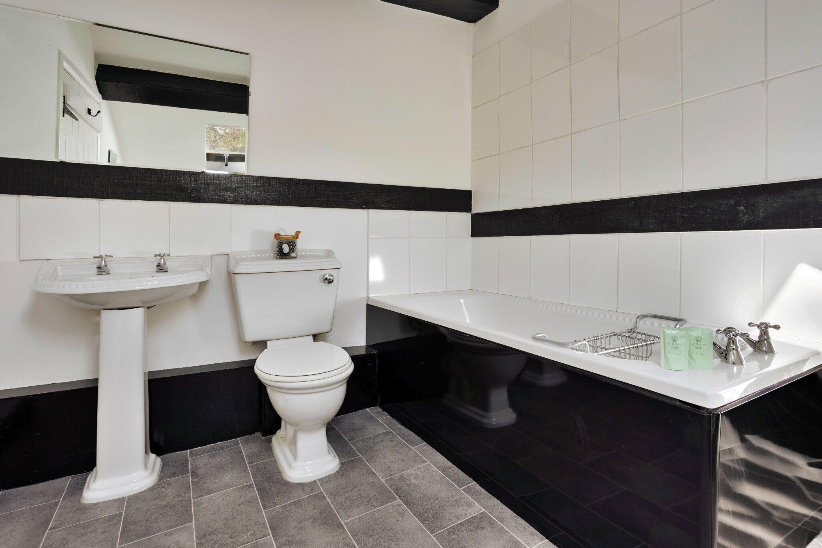 Un baño con lavamanos, inodoro y bañera blancos, todos con detalles en negro.