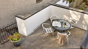 An outdoor patio with a round table, two chairs, a potted plant, and a metal fence. - Charming Snowdonia Cottage for 4 (Ambleside)