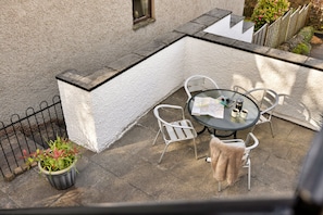 Eine Terrasse im Freien mit einem runden Tisch, zwei Stühlen, einem Blumentopf und einem Metallzaun.