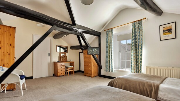A bedroom with two beds, a wooden dresser, a desk, and a chair. There is a window with patterned curtains and a framed picture on the wall. - Charming Snowdonia Cottage for 4 (Ambleside)