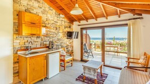 Une cuisine aux murs en pierre, aux armoires en bois et dotée d’une grande fenêtre donnant sur un balcon avec vue sur la mer.