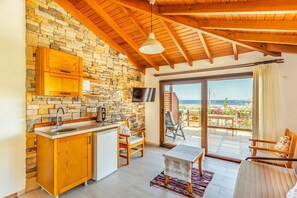 Una cocina con paredes de piedra, armarios de madera y un amplio ventanal con vistas a un balcón frente al mar.