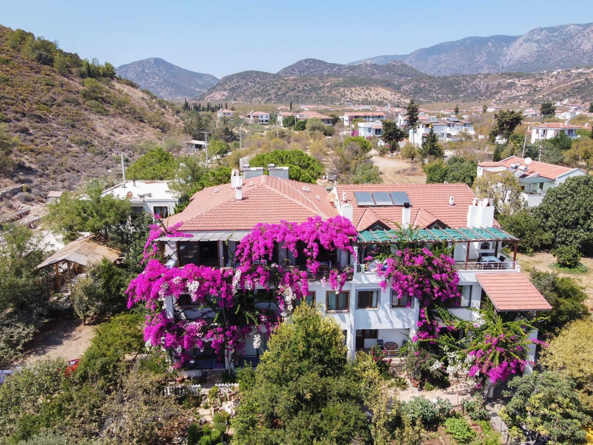 A residential building with a red-tiled roof, surrounded by lush greenery and flowering plants.