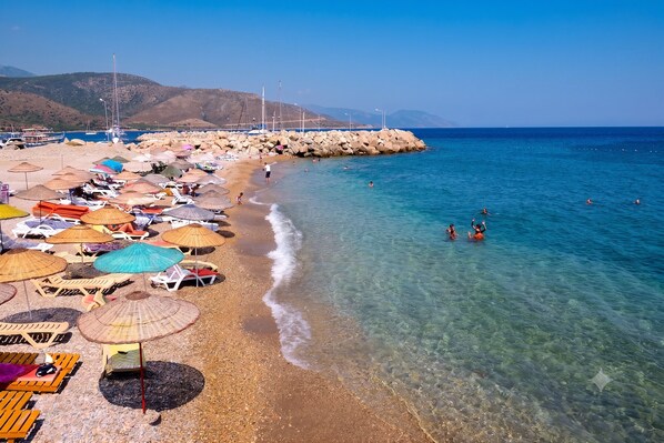 A beach with clear water, umbrellas, and sun loungers. - Liman Pansiyon Palamutbükü (Datca)