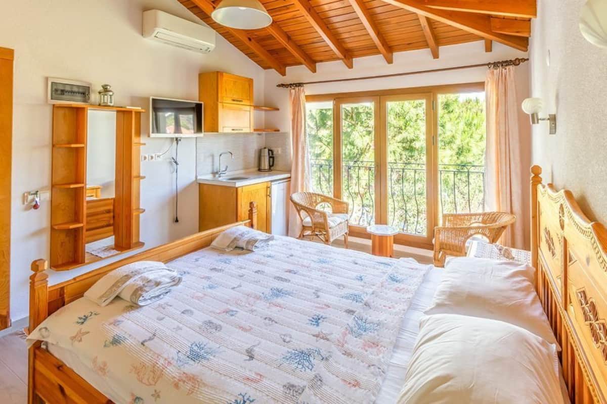 Un dormitorio con una cama grande, muebles de madera, un televisor y un balcón con vistas a zonas verdes.
