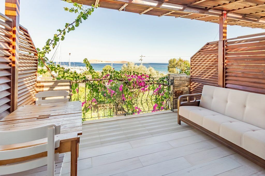 A covered outdoor seating area with a view of the sea, a white sofa, and a wooden table.