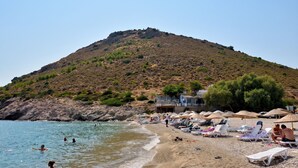 A beach with people swimming and sunbathing, a hill in the background, and a building with a balcony overlooking the beach.