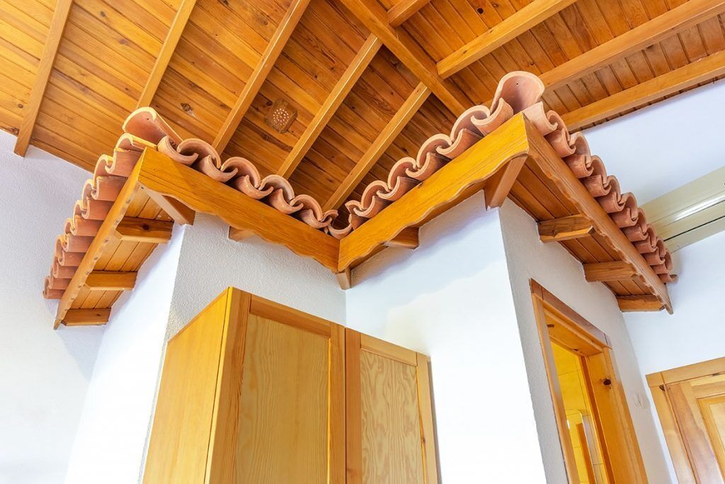 A room with wooden ceiling beams, a terracotta cornice, and wooden doors.