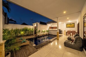A modern outdoor living area with a swimming pool, a dining area, and a kitchen. - Villa Gede Seminyak (Badung)