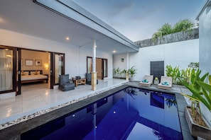 A modern indoor pool area with a glass enclosure, a bed, seating, and potted plants. - Villa Gede Seminyak (Badung)