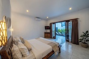A bedroom with a bed, a TV, and a sliding glass door leading to a balcony. - Villa Gede Seminyak (Badung)