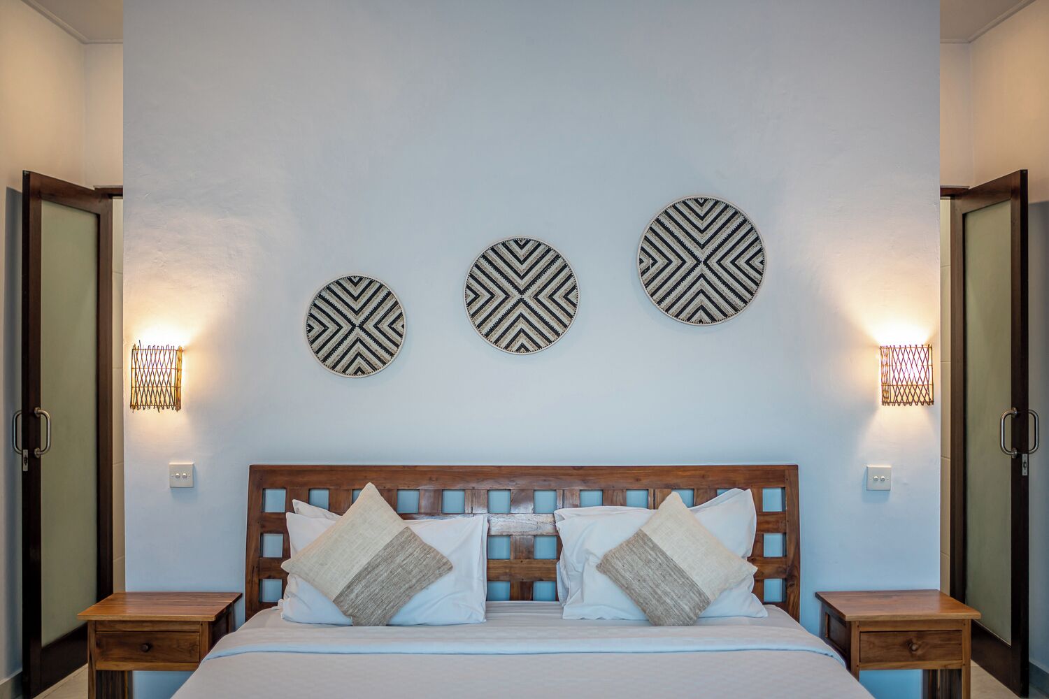 A bedroom with a wooden headboard, a bed with white linens, and three wall-mounted circular decor pieces.