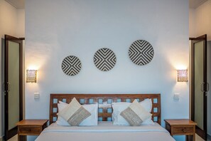 A bedroom with a wooden headboard, a bed with white linens, and three wall-mounted circular decor pieces. - Villa Gede Seminyak (Badung)