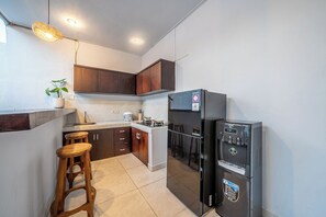 A compact kitchen with dark wooden cabinets, a black refrigerator, a gas stove, and a bar stool. - Villa Gede Seminyak (Badung)