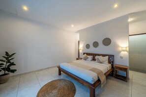 A bedroom with a bed, bedside tables, wall decor, and a potted plant. - Villa Gede Seminyak (Badung)
