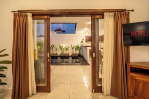A room with a sliding glass door leading to a balcony, a flat-screen TV, and a view of the sky. - Villa Gede Seminyak (Badung)