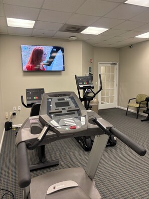 Una sala de fitness amb esteques, una televisió que mostra una dona cantant, i una porta al fons.