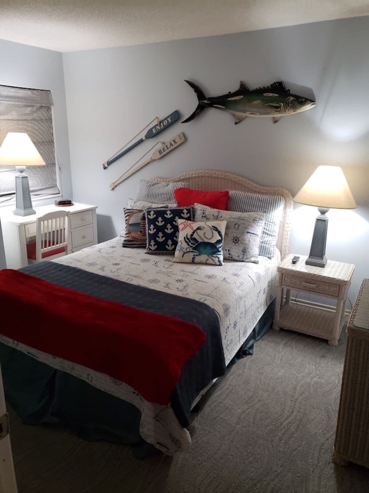 Un dormitorio con cama, dos mesitas de noche, un pez colgado en la pared y decoración náutica.
