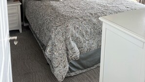 Un dormitorio con panel de pared de madera, cabecera blanca, colcha estampada y ventilador de techo.