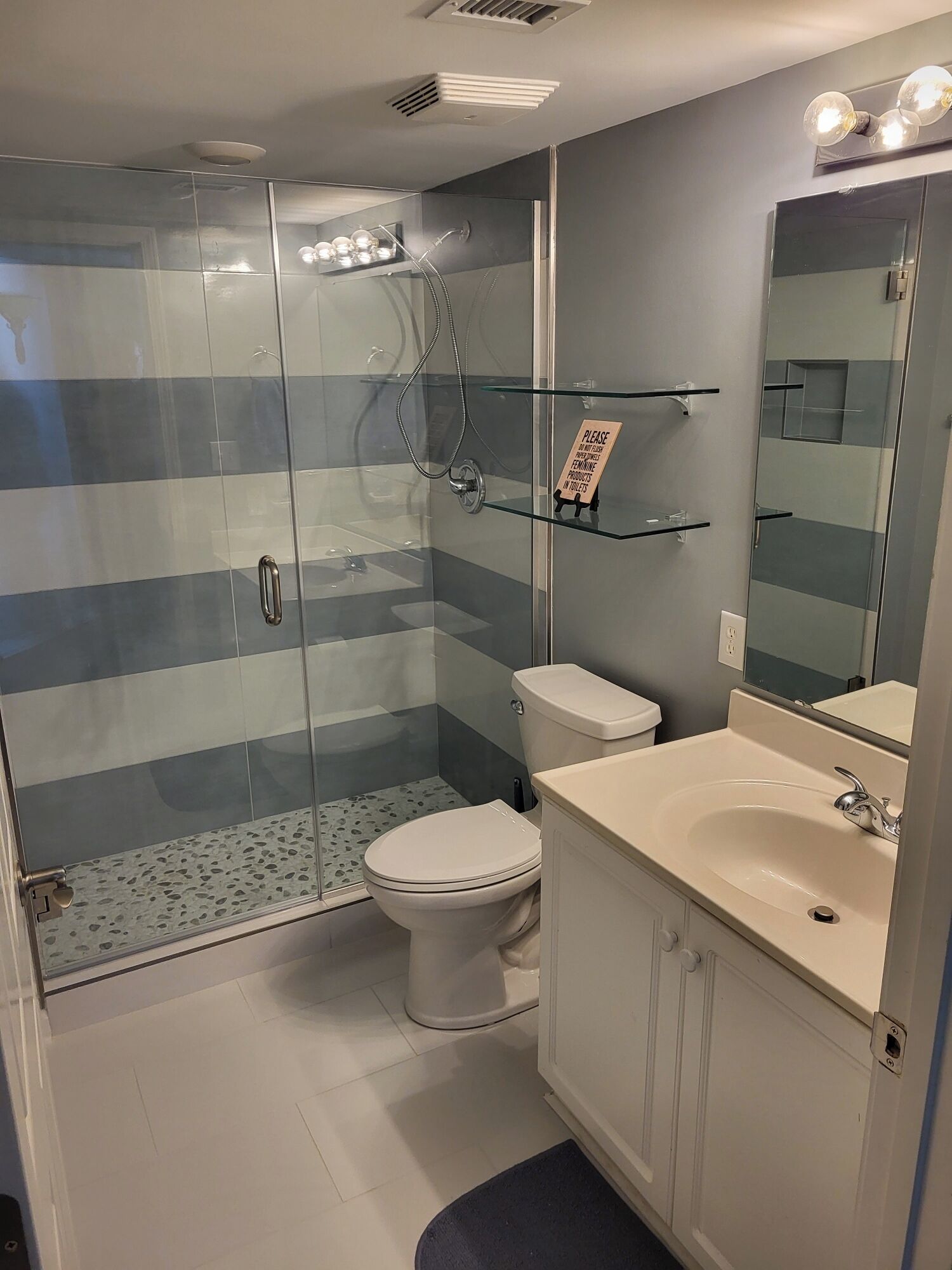 Ein modernes Badezimmer mit einer gläsernen Duschkabine, einer Toilette und einem Waschtisch mit Spiegel.