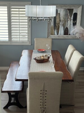 Un comedor con mesa de madera, sillas acolchadas, un banco, un cuenco decorativo y una lámpara colgante.