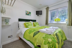 A neatly made bed with a green leaf-patterned bedspread, a flat-screen TV on the wall, and a window with curtains. - Luxury Country Estate Near Largs (Betws-Y-Coed)