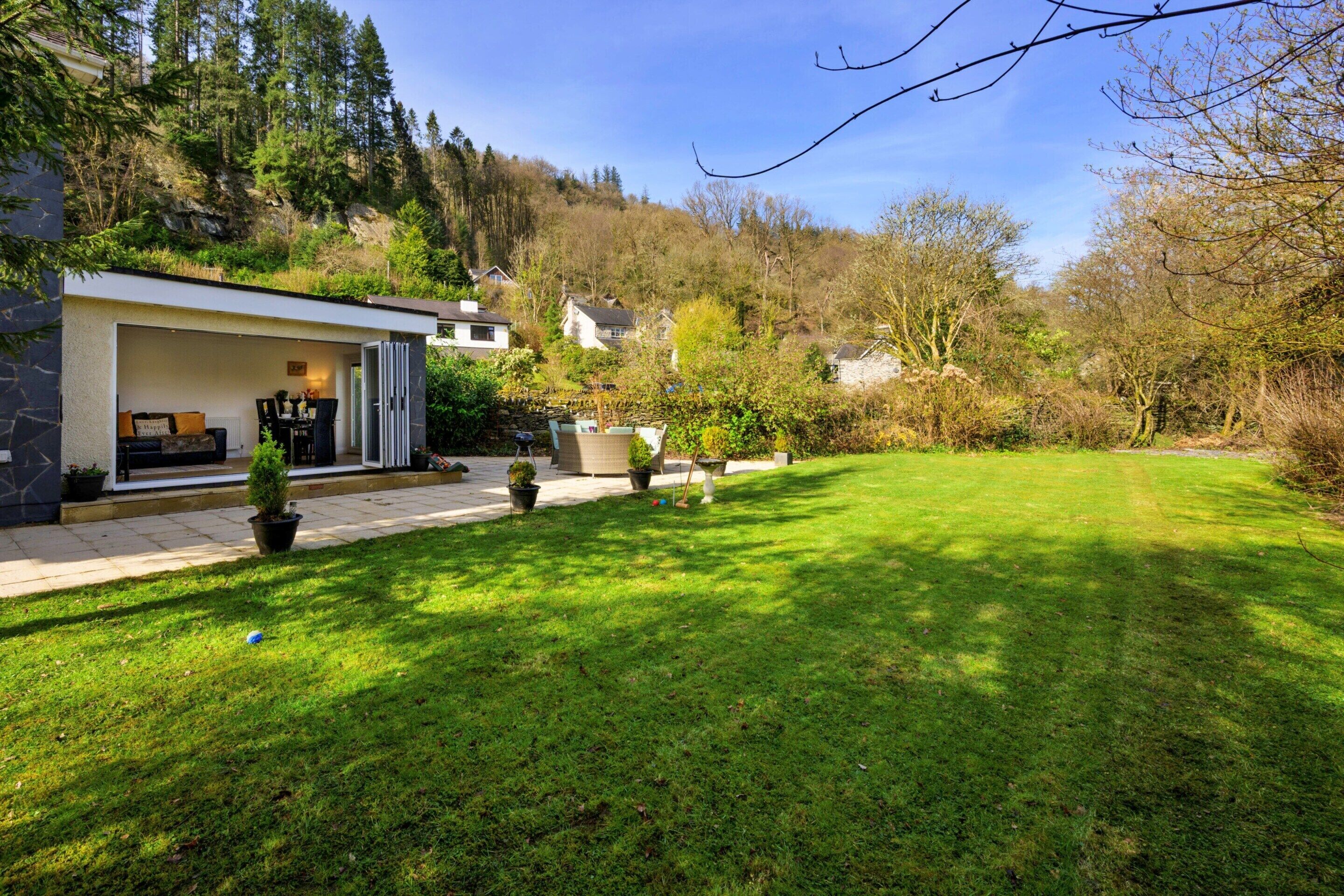 A modern house with a covered outdoor seating area, a well-maintained lawn, and a stone wall.