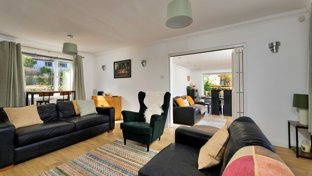 Ein modernes Wohnzimmer mit Sofa, Sessel und einem Essbereich, der durch eine offene Tür sichtbar ist.